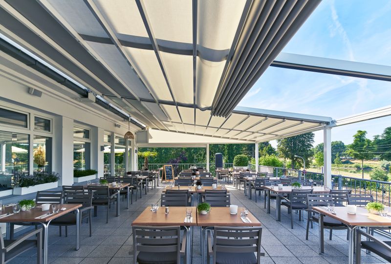 Reference image of a semi-extended pergola stretch in cream over the outdoor area of the "bootshaus" in Mannheim, Germany